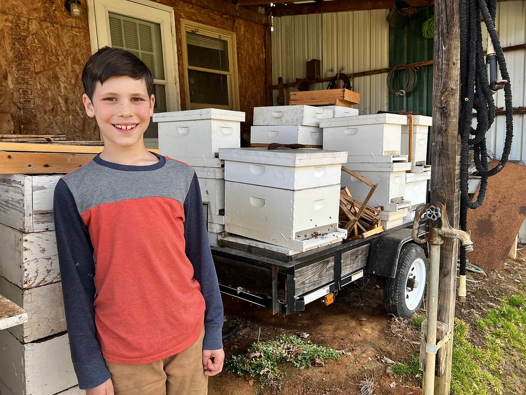 9 year old boy next to honey bee boxes