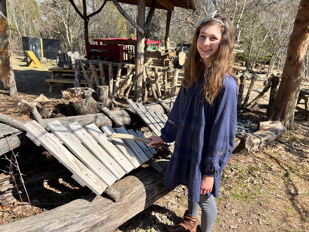 teen girl playing with wooden xylophone outside