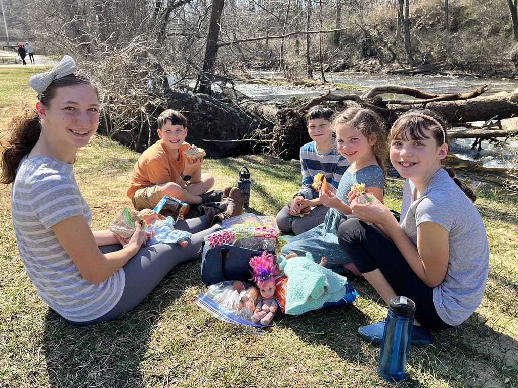 five siblings having a picnic by the river in early spring