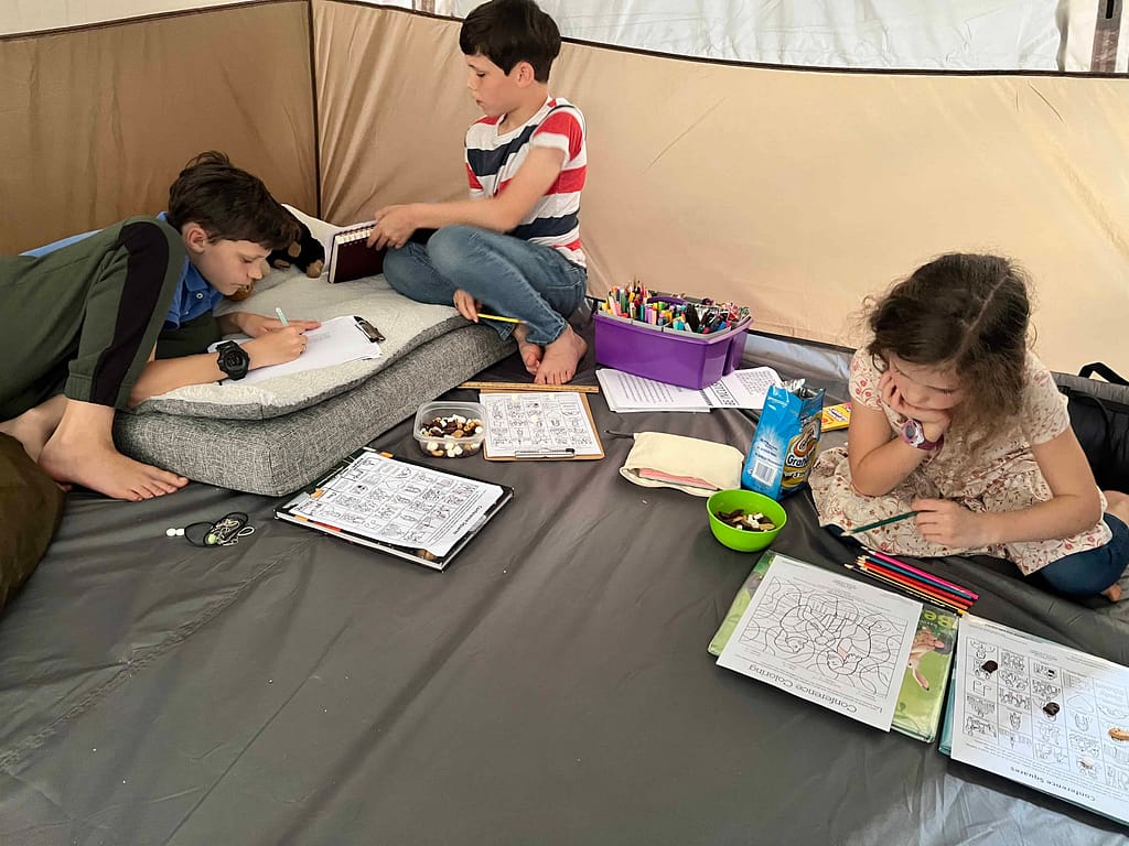 3 kids drawing in a tent
