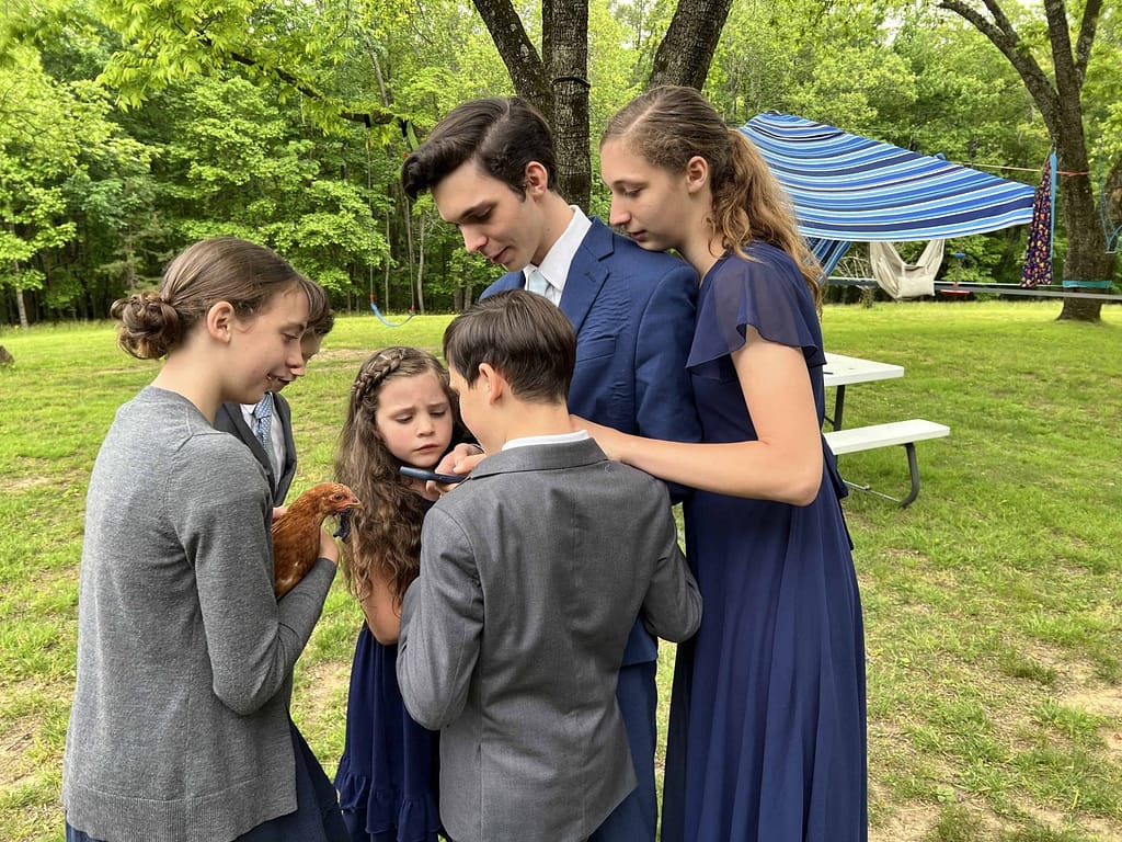 siblings looking at big brother's phone over his shoulder