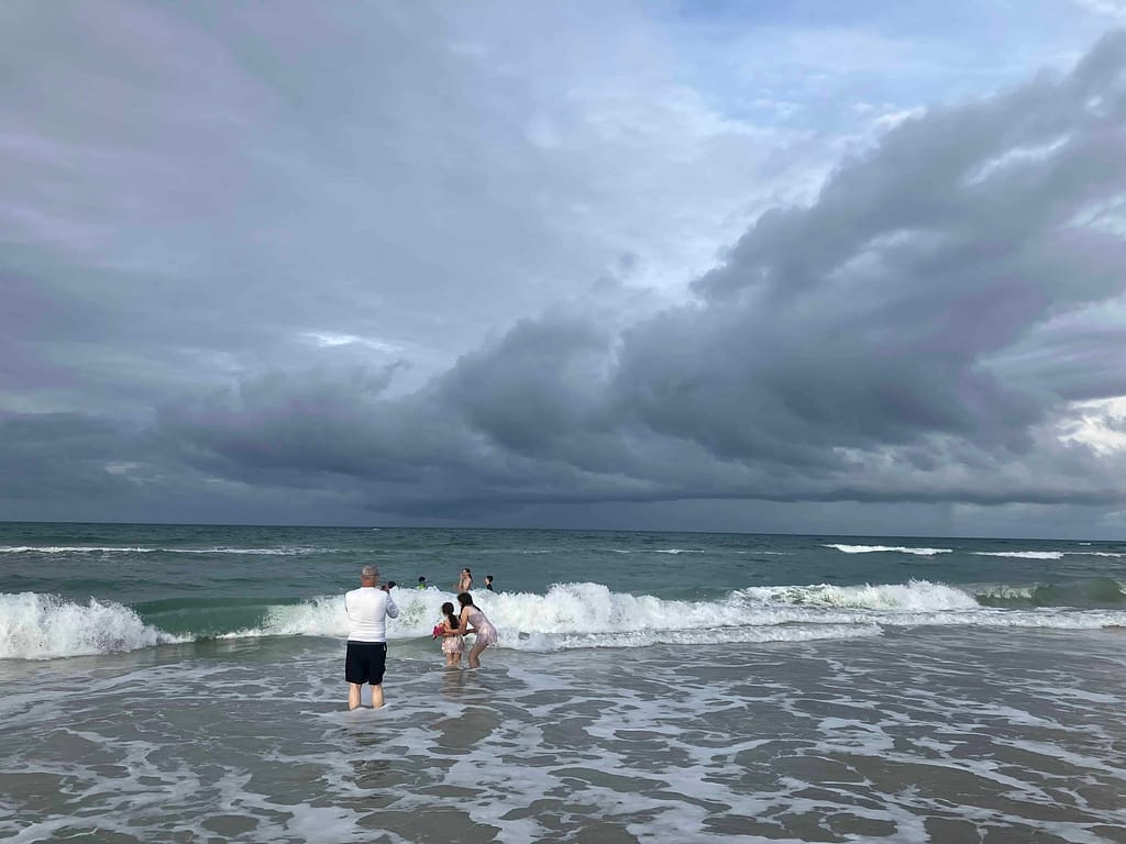kids swimming in the ocean with big clouds overhead