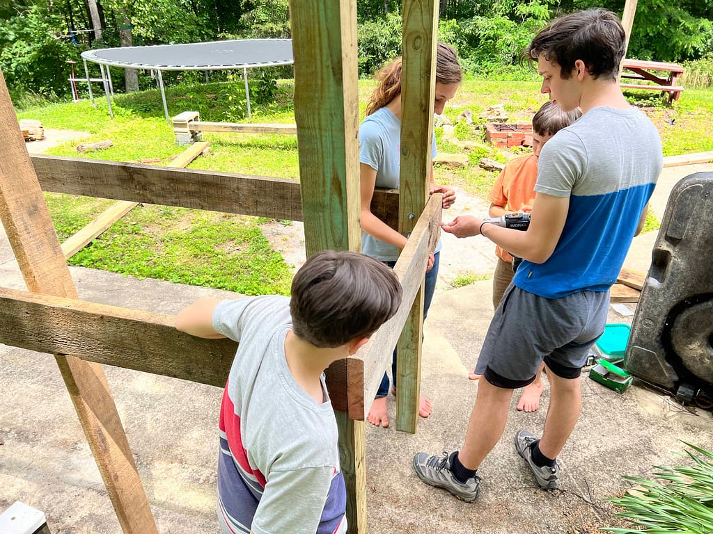 siblings building a wooden obstacle course and screwing it in