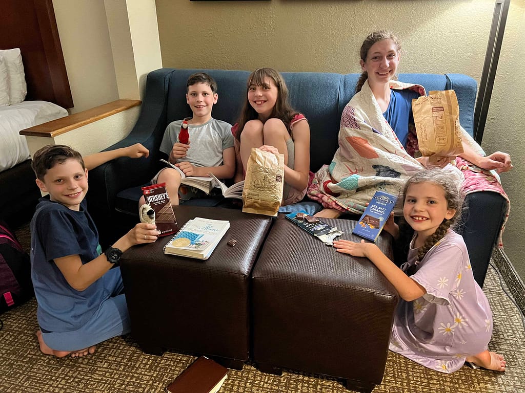5 siblings eating popcorn and chocolate on a couch at a hotel