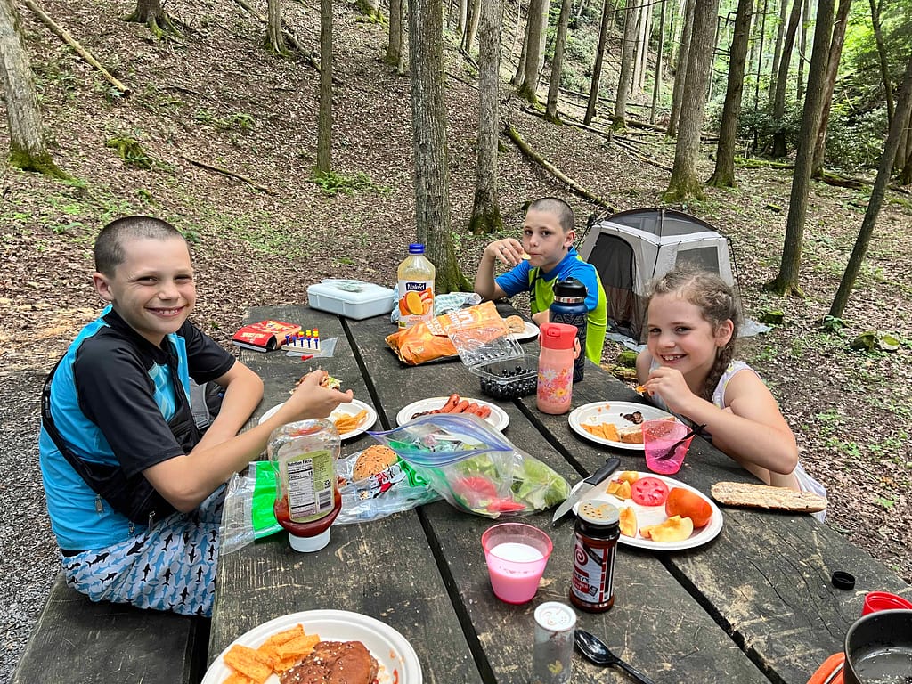 three kids eating dinner at a campsite in their swimsuits