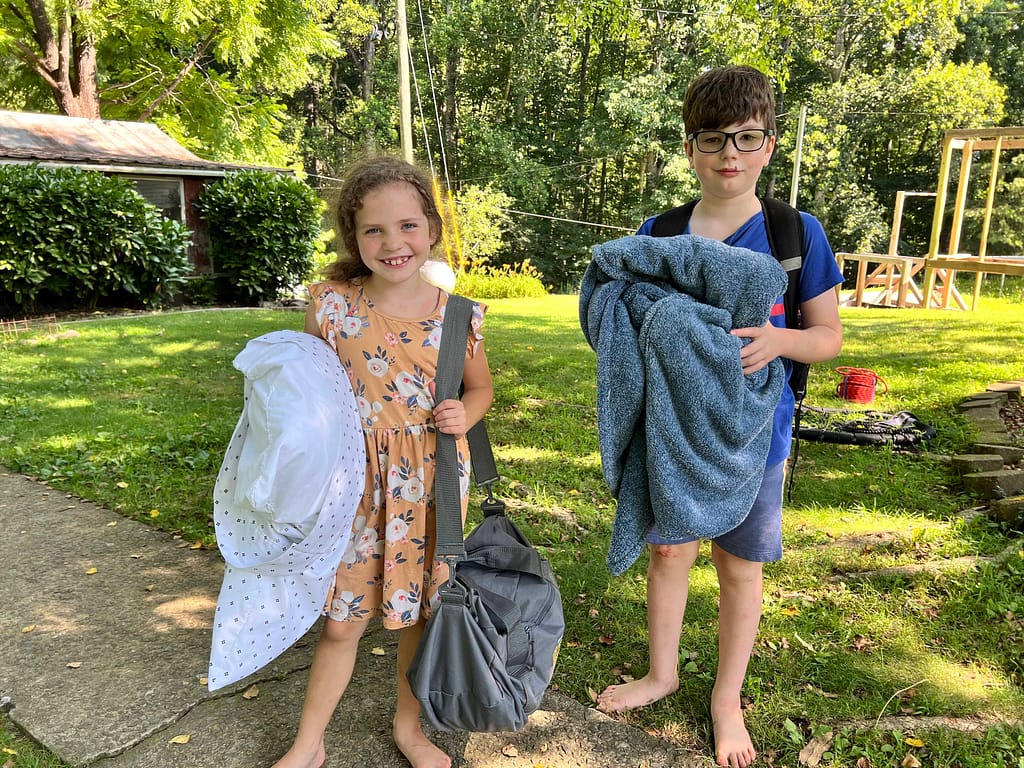two kids carrying pillows and duffle bags
