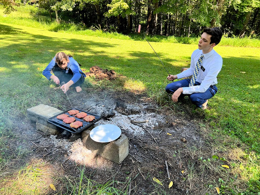 two siblings roasting hot dogs in coals