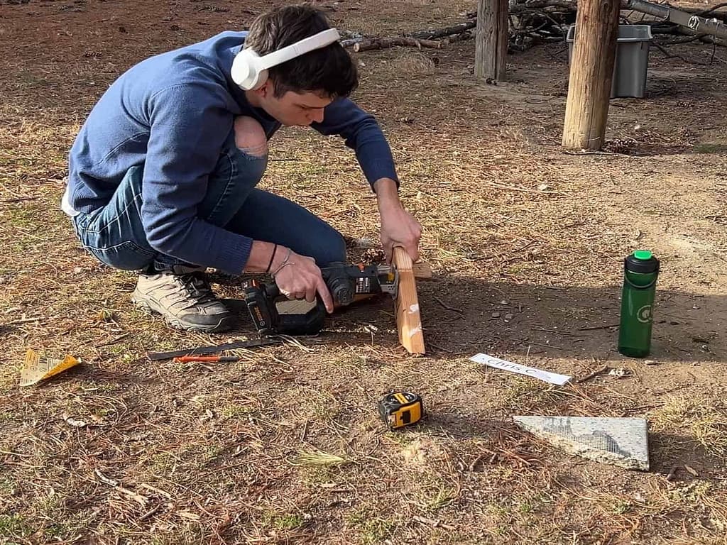 teen boy using hand saw to cut wood
