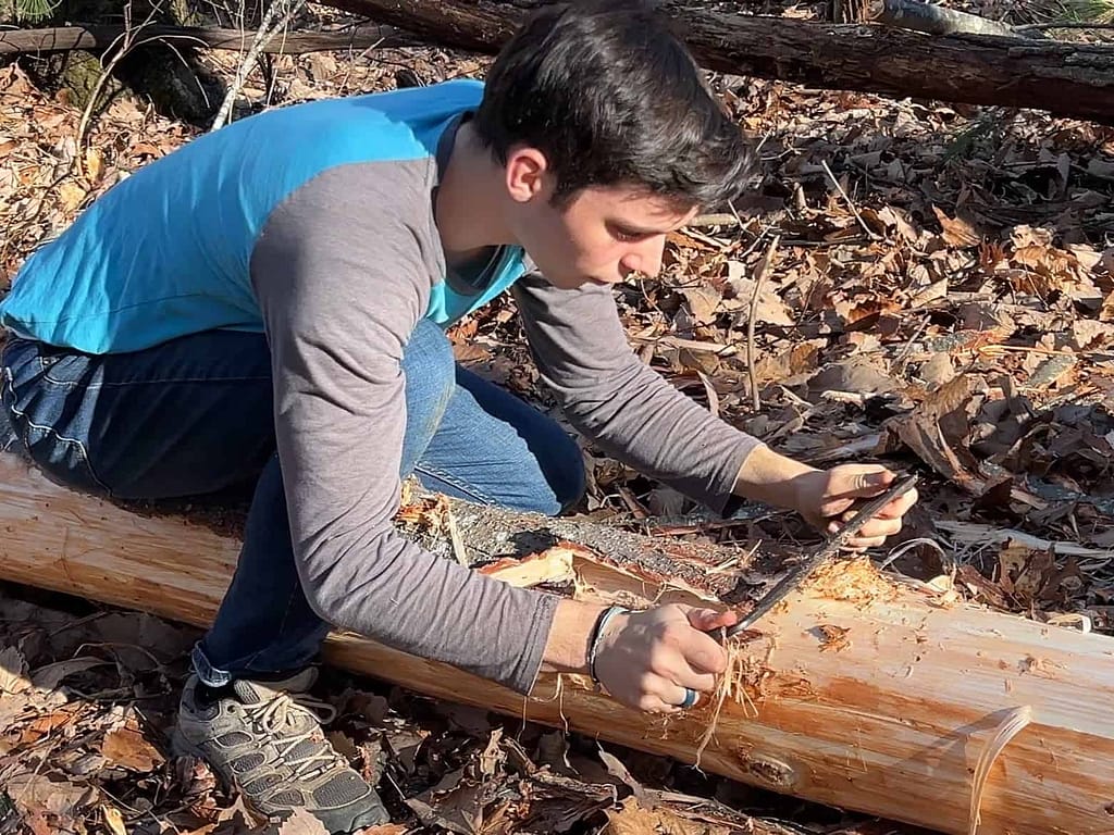 young man stripping bark off log