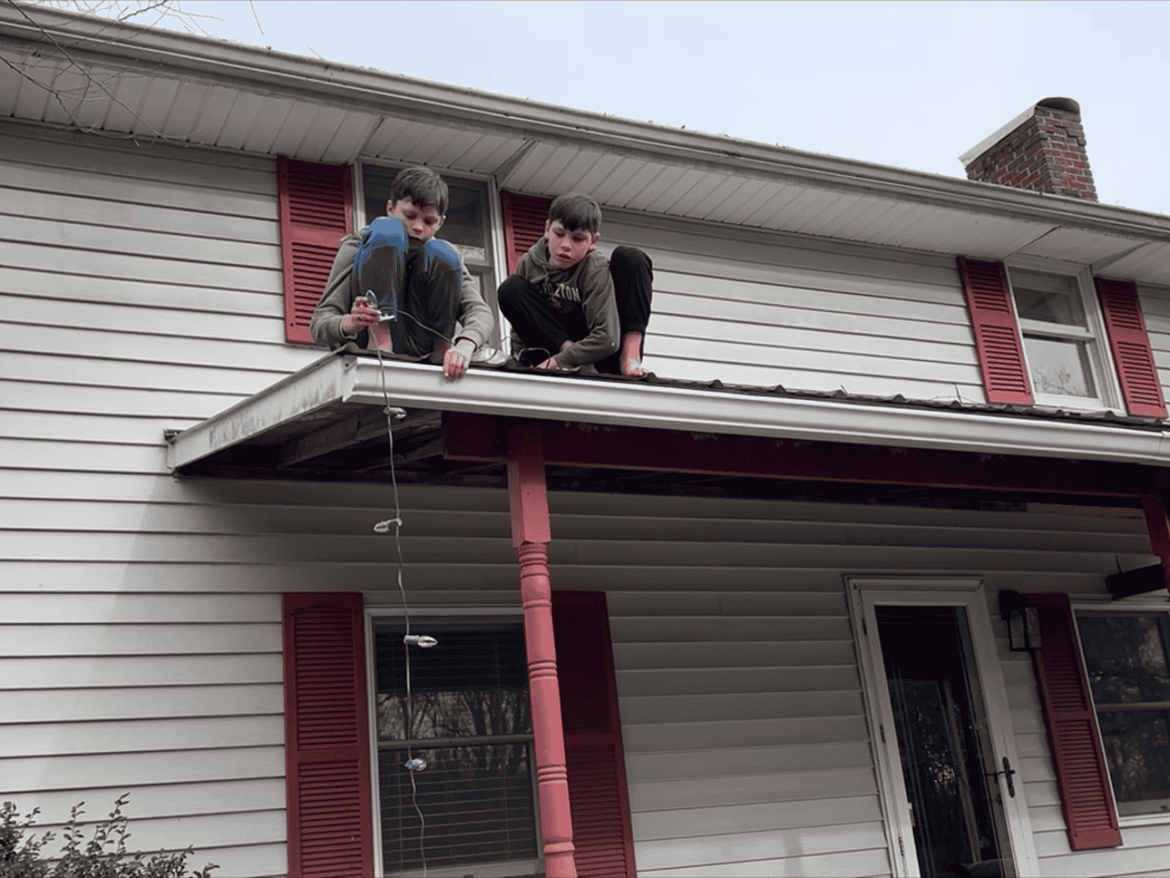 two boys putting lights on the roof of a farmhouse