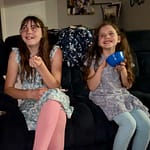 two sisters eat popcorn and watch a movie on the couch