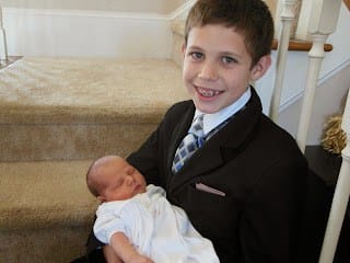 10 year old brother holding baby brother dressed in white