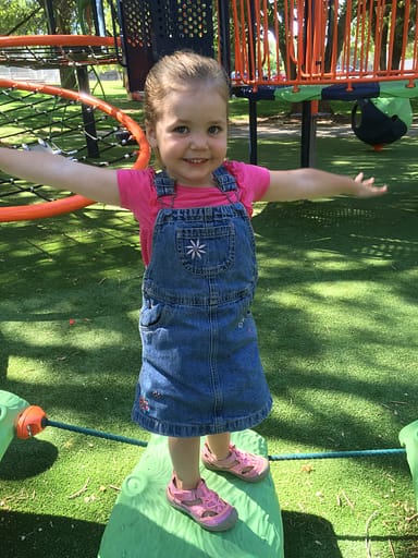 little girl standing on a toy at the park with her arms outstretched