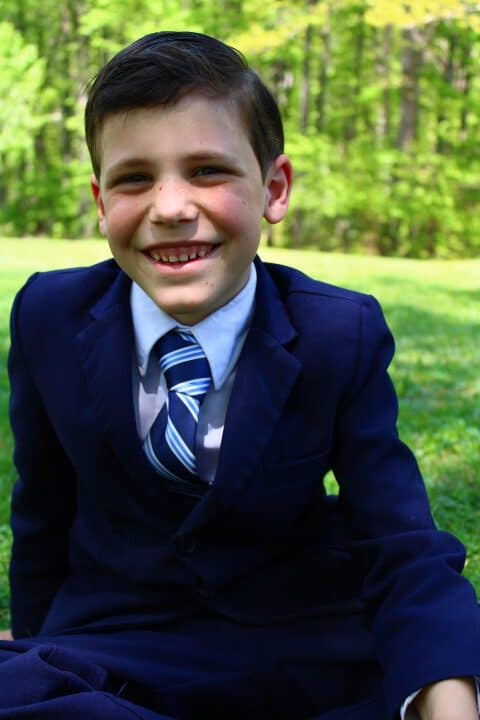 sever year-old dressed up in a navy blue suit and tie.