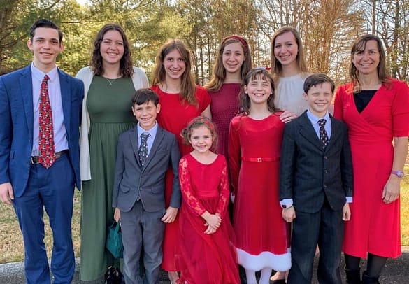 family of 9 kids and their mother dressed in Sunday best Christmas colors on Christmas Eve. Outside on a beautiful day