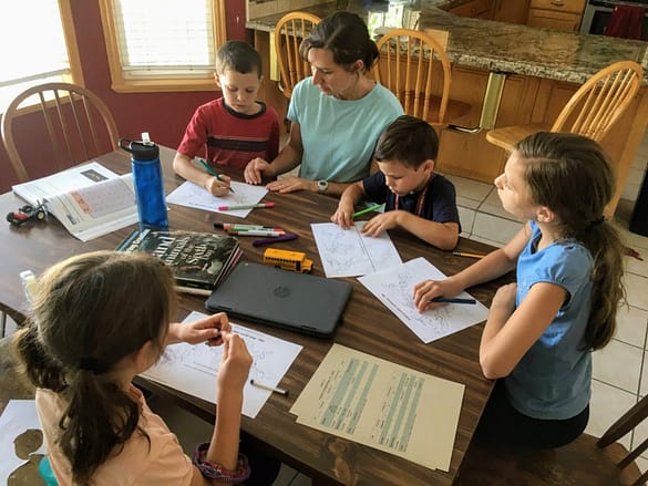 A mom helps her kids with homeschool around the table.