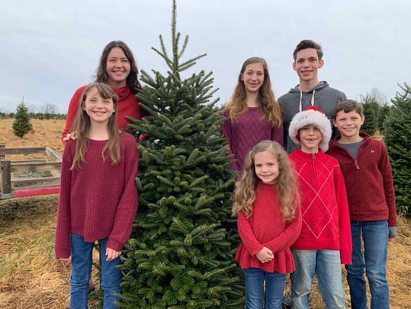 family of 7 kids standing by a tree at a christmas tree farm
