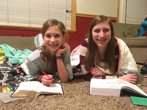 two sisters reading their scriptures on the living room floor