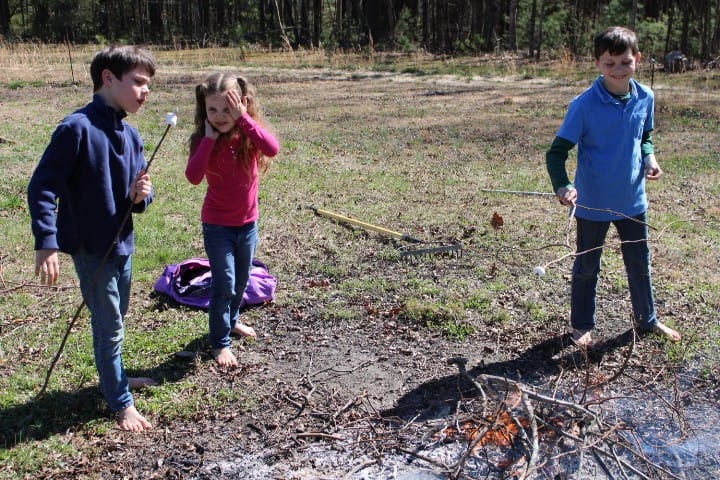 three little kids looking at their marshmallows as they cook them.