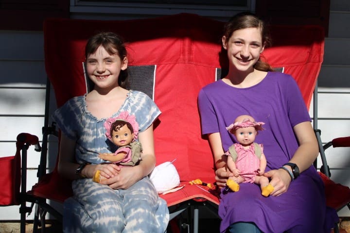 two girls sitting on the porch with their matching dolls