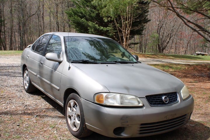 Gold Nissan car sitting in a rural driveway.