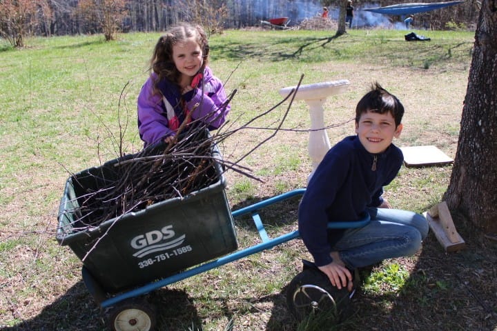 boy riding hoverboard and loading sticks into the cart he's pulling with his little sister helping him.