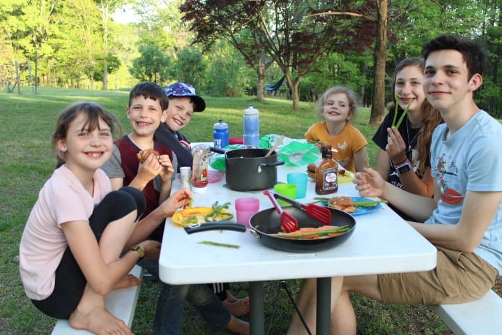 Family of 6 kids eating sloppy joes and asparagus at a picnic table in spring.