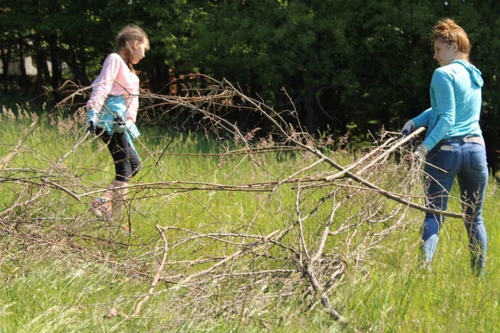 An 11 year-old and 17 year old girl grab dead branches to haul them to a burn pile.