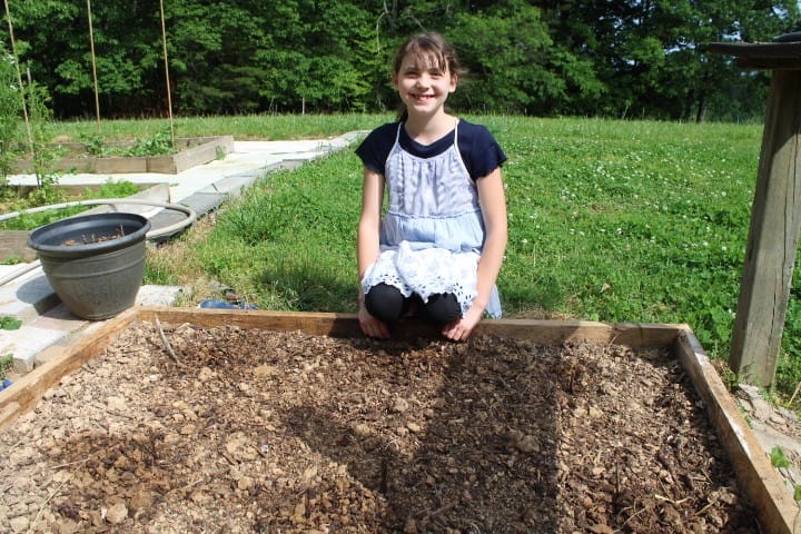 11 year old kneeling by a garden bed she planted