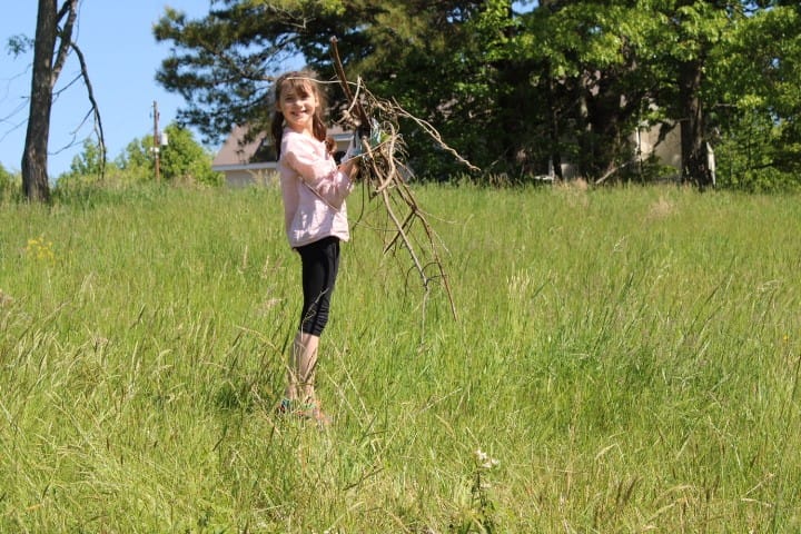 11 year-old smiles while carrying branches to a burn pile in a big grassy field.