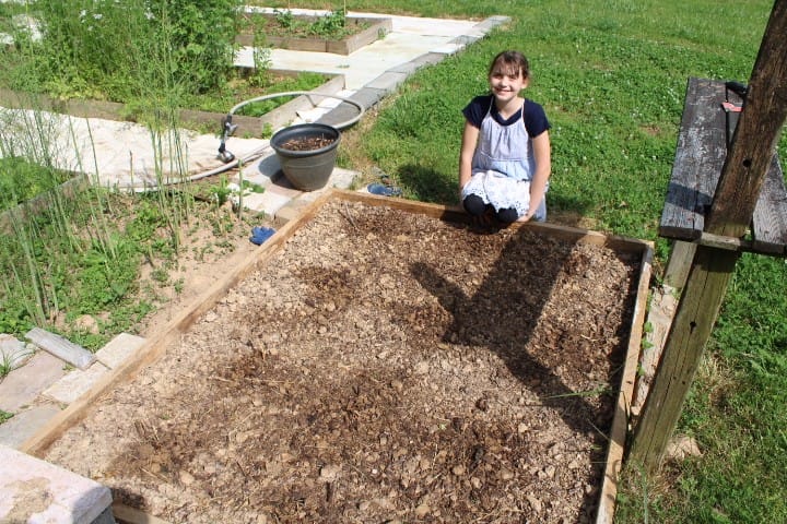 11 year old kneeling by a garden bed she planted