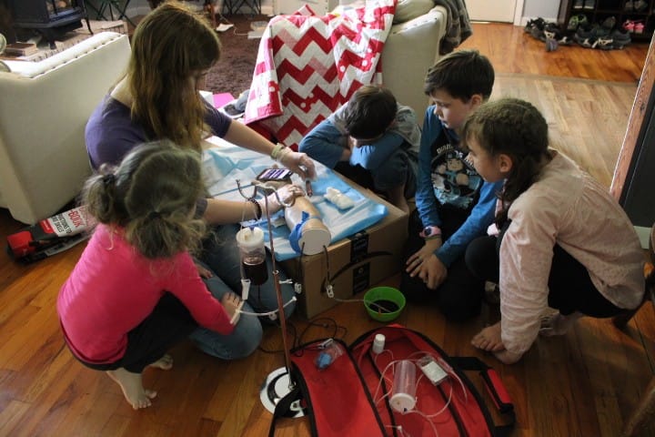 a 17 year old shows younger siblings how to do a blood draw on a fake arm.