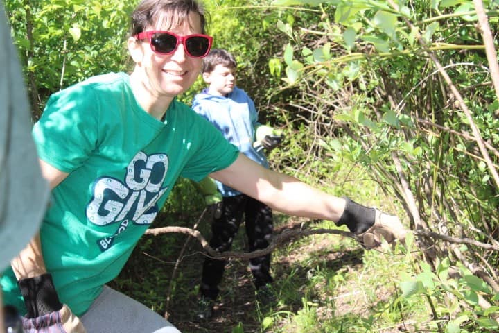 A mom pulls out a stubborn vine from a blueberry patch and smiles at the camera.
