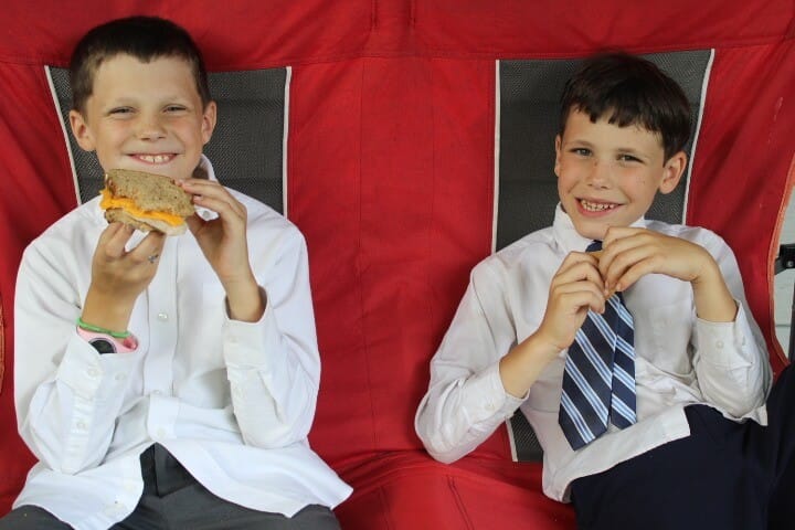 two boys eating sandwiches in their church clothes on the front porch