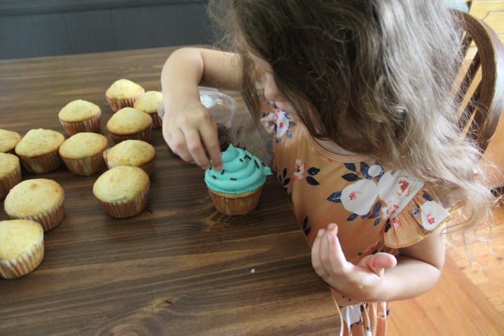 girl puts sprinkles on her cupcakes