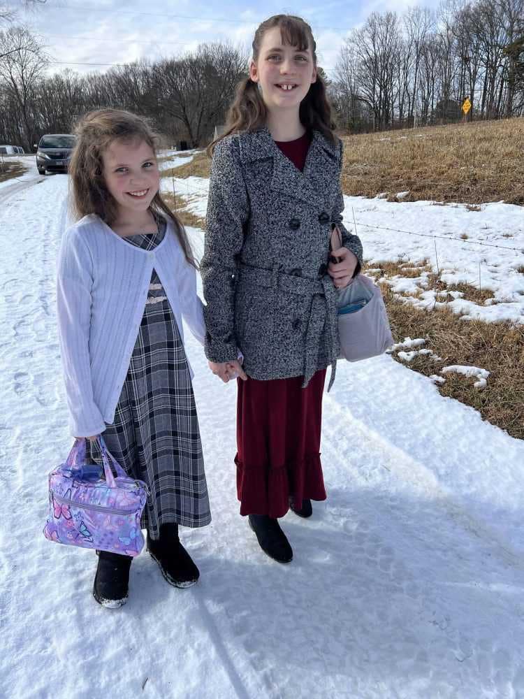 two girls walking in the snow in church dresses