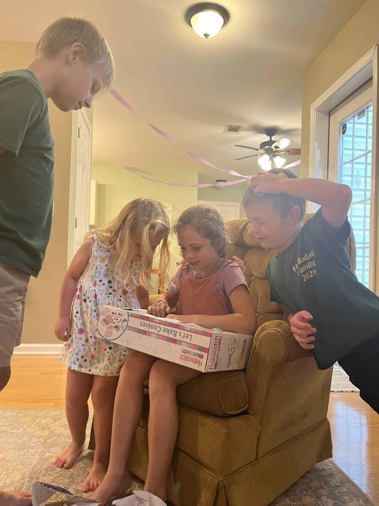 girl opening presents with cousins watching