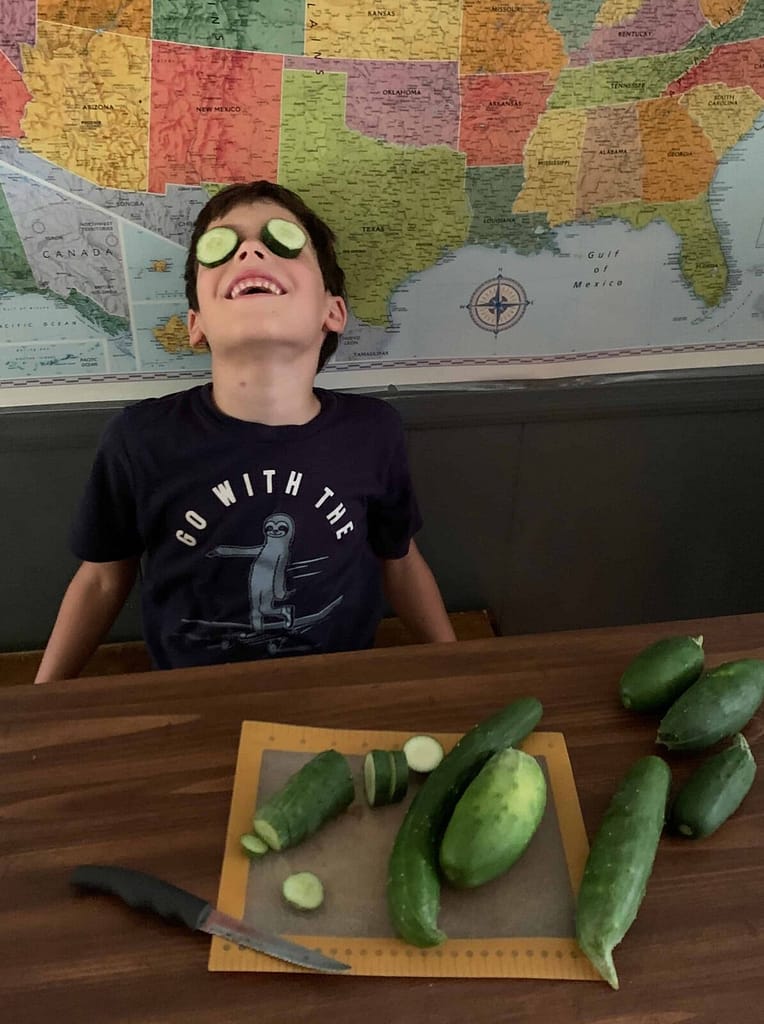 a boy with cucumbers on his face while cutting them