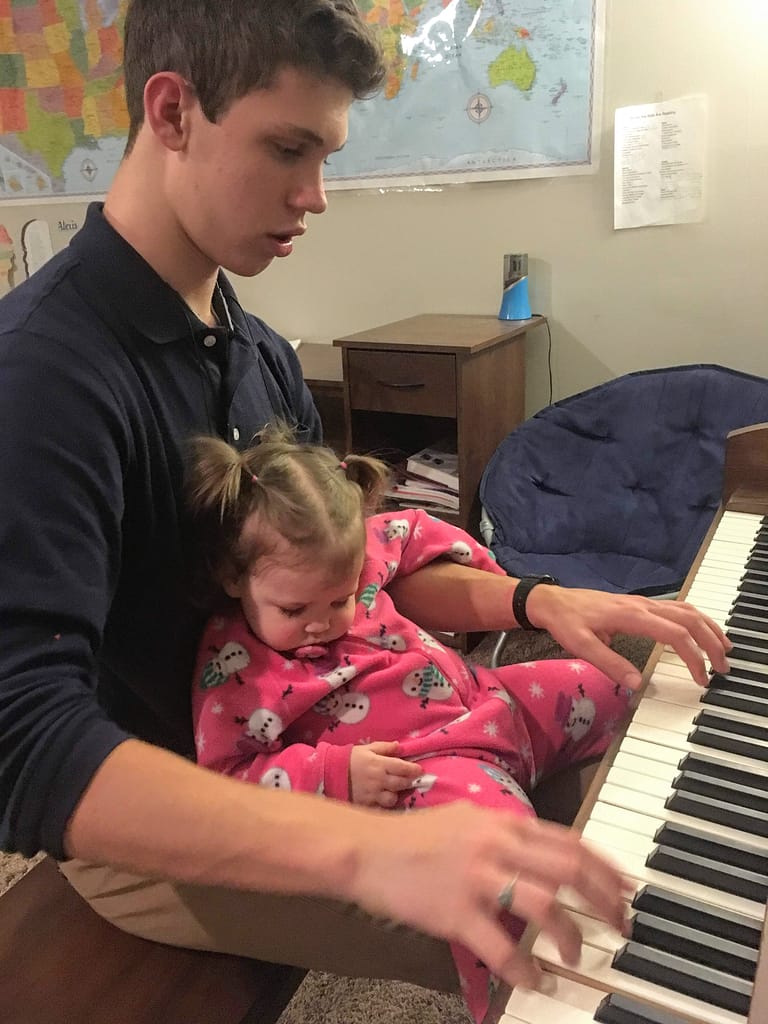 Baby girl falls asleep in her brothers arms as he plays the piano.