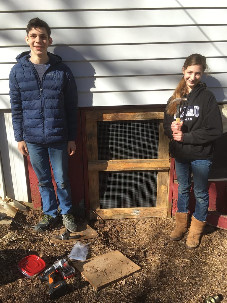 two siblings stand by the chicken coop door they built together