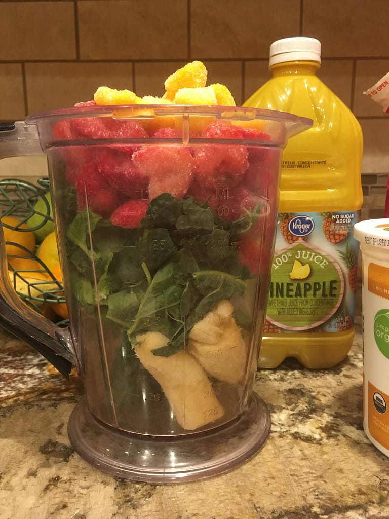 blender full of ingredients for a juice shake. bananas, strawberries, kale, and mango.