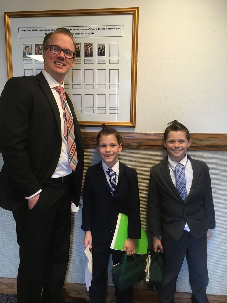 Two little boys with suits standing by a guy at church with a suit.