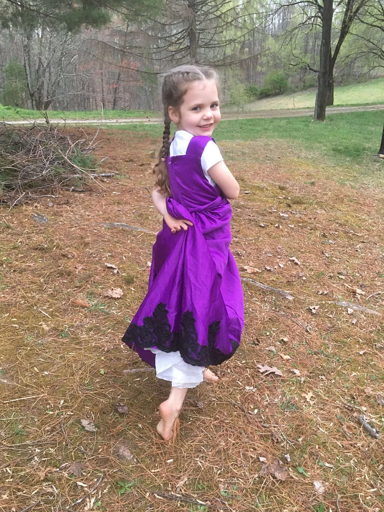 A 5 year old twirling in her purple princess dress outside.
