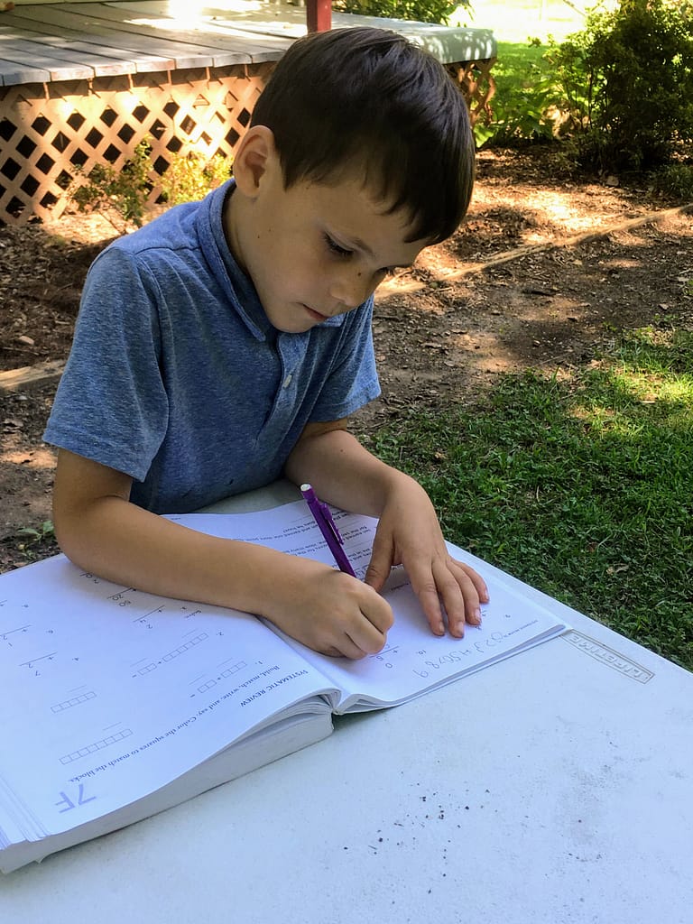 6 year old does his homeschool math outside on the picnic table