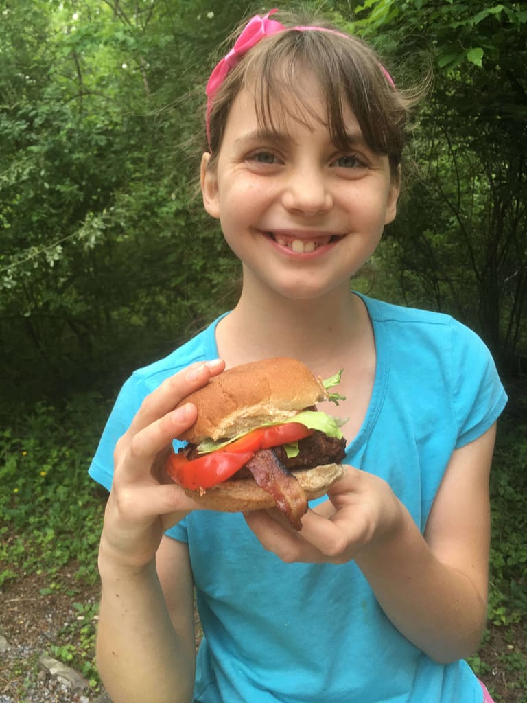 11 year old girl showing a bacon hamburger she made camping