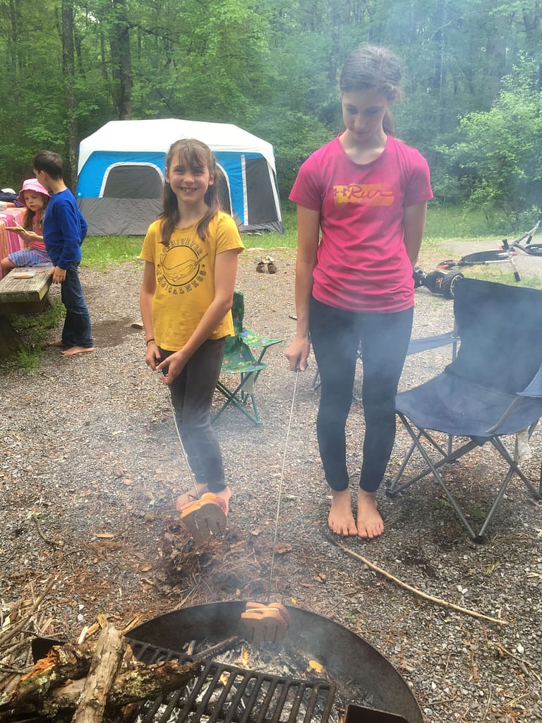two sisters cooking grilled cheese in a stick at a campfire