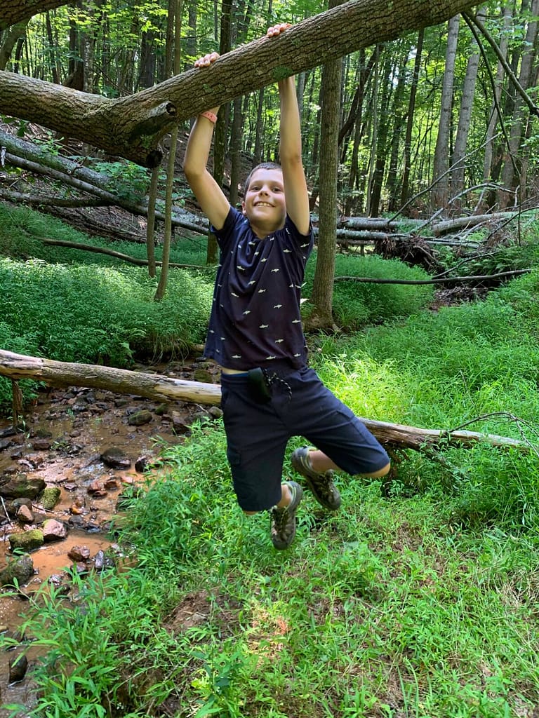 boy doing pull up on a fallen tree across a creek
