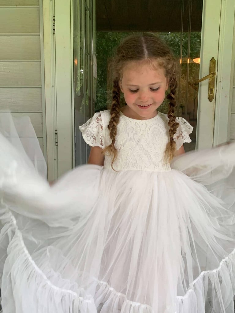 little girl holding her white dress out on both sides of her