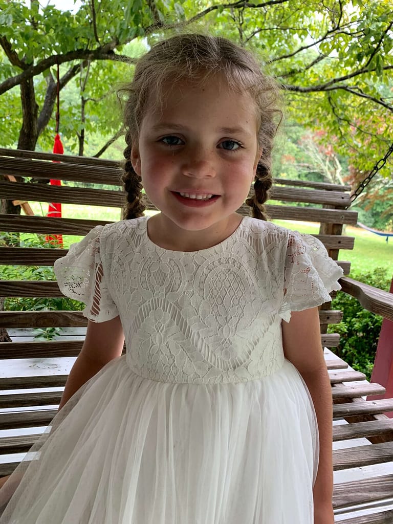 6 year old sits on the porch swing with a white dress on