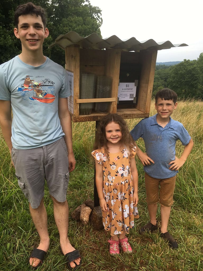 3 kids stand by a finished blueberry stand cash box